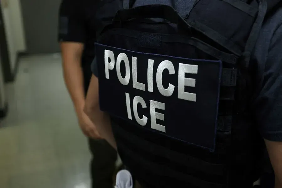 Close view of a dark vest with white 'POLICE ICE' lettering, person's back turned.