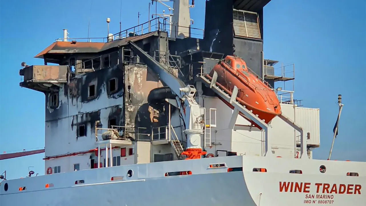 Fire-blackened tanker ship Wine Trader with scorched superstructure and orange lifeboat visible.