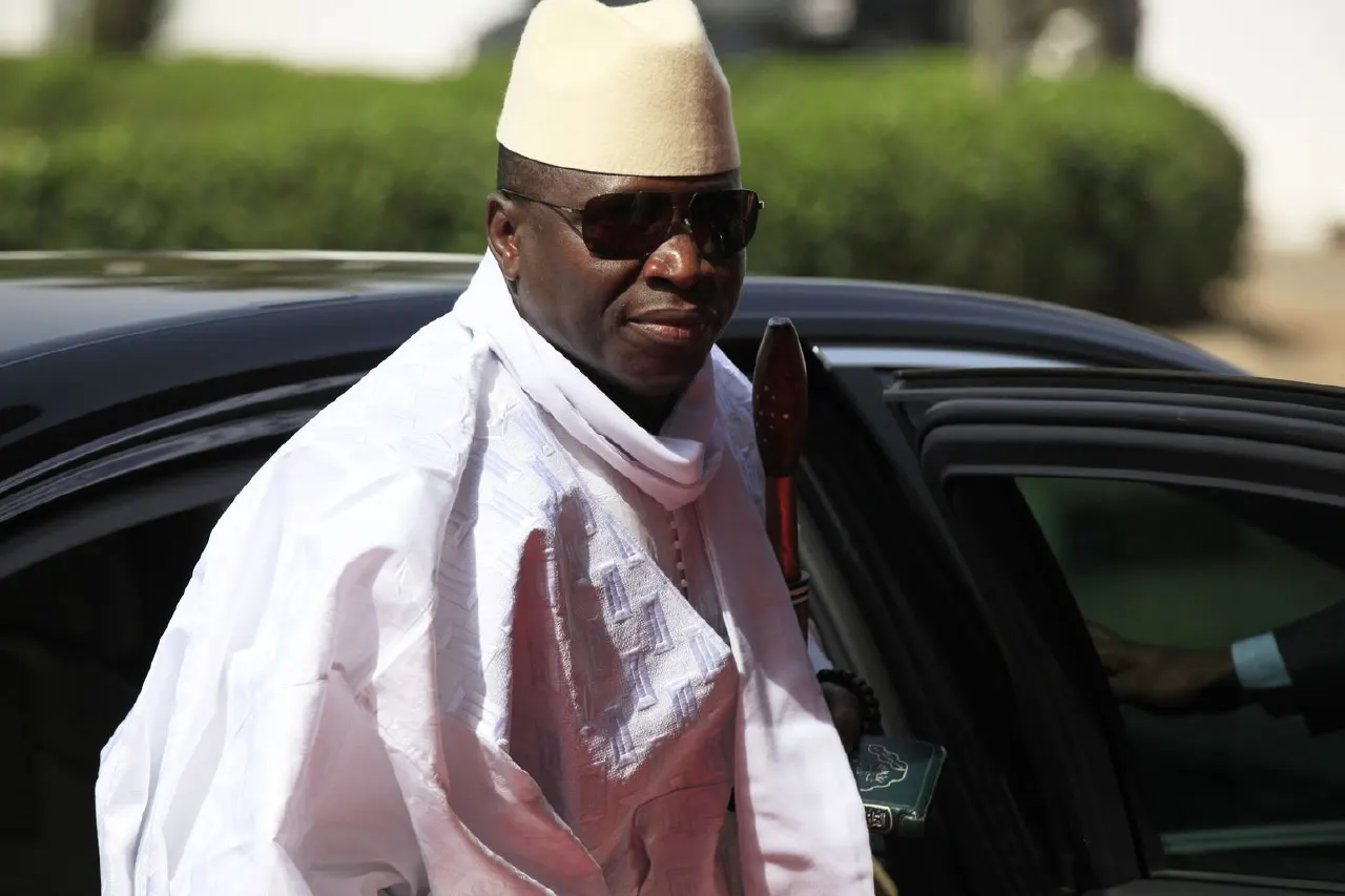 Man in white traditional robes and cream cap and sunglasses stepping out of a dark car.
