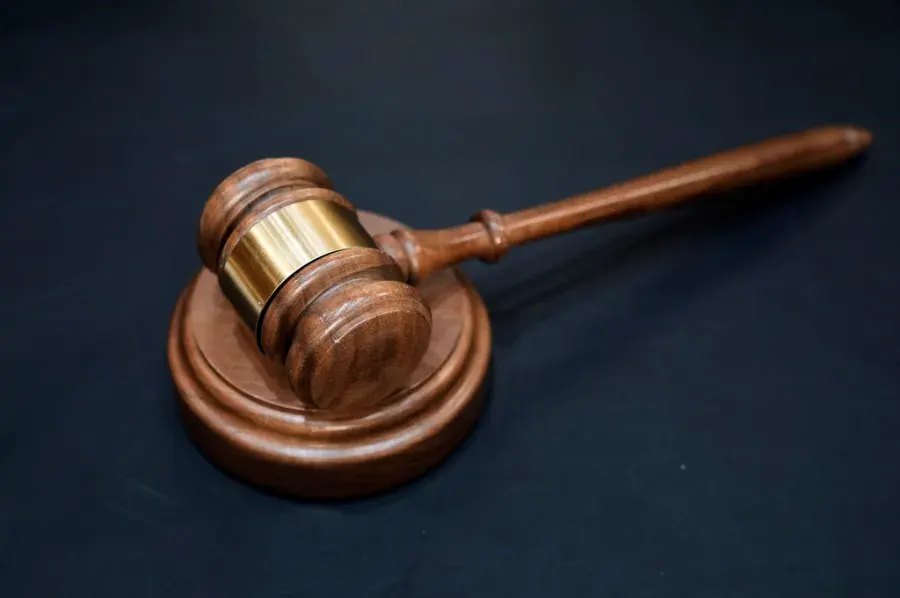 Wooden judge's gavel on a round block against a dark background, suggesting courts and law.