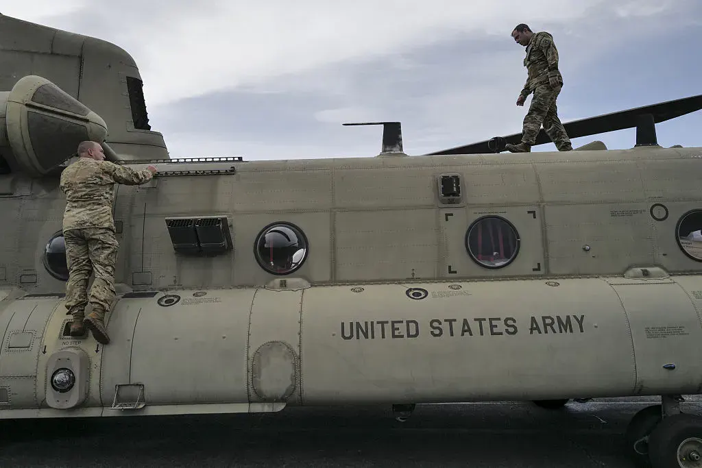 Two soldiers in camouflage climb a US Army Chinook helicopter on a tarmac