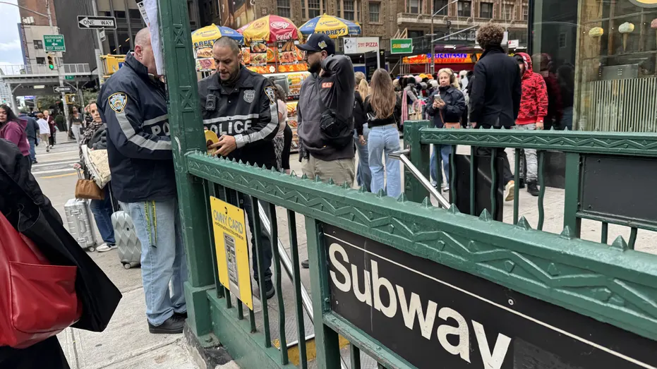 Officers in NYPD-style jackets stand near a green subway entrance marked Subway on a busy city street.