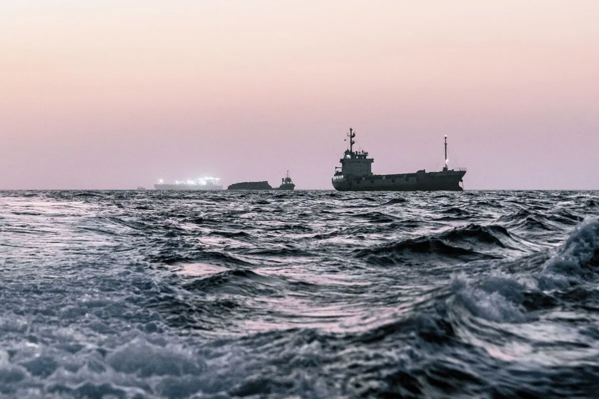 Cargo ships on choppy sea at dusk, with waves in the foreground.