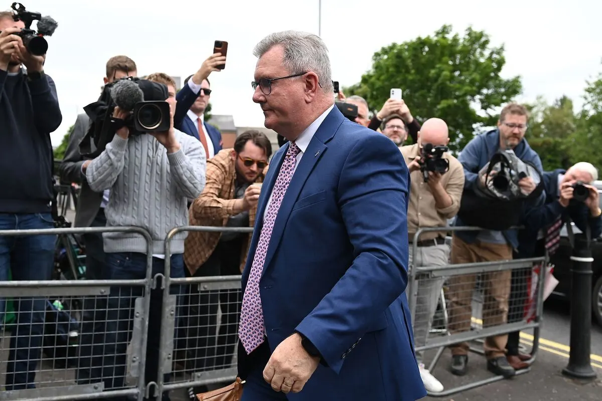Man in blue suit walks past press photographers and cameras along a street barrier.