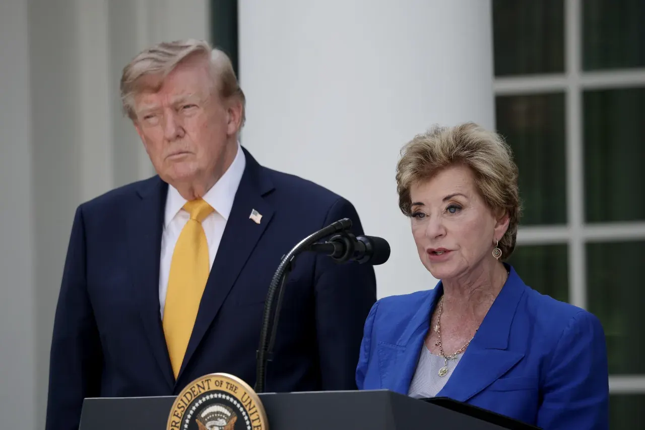 Two people at a lectern with a presidential seal, one man standing behind a woman speaking