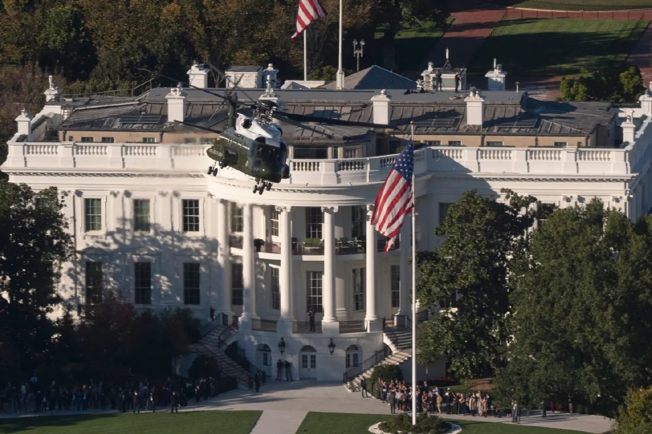 Helicopter lifting off near the White House South Portico, with American flags and onlookers.