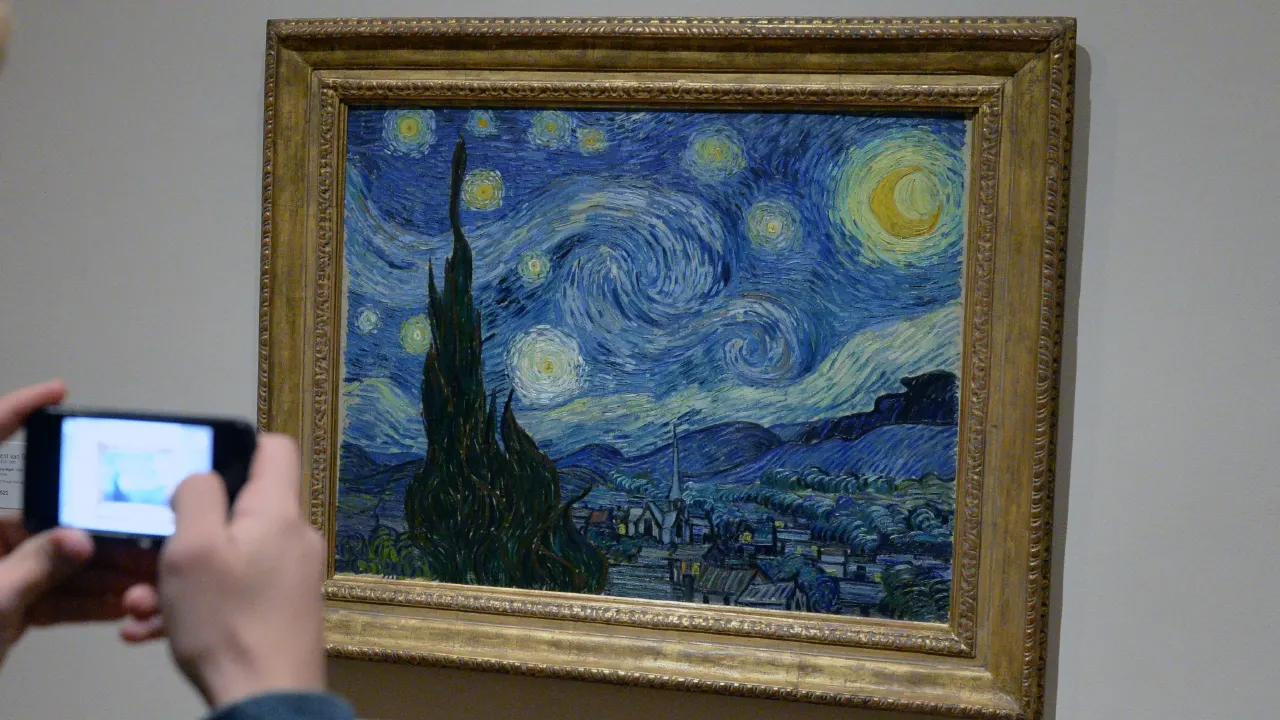 Person photographing van Gogh's Starry Night painting in a gilded frame on a gallery wall