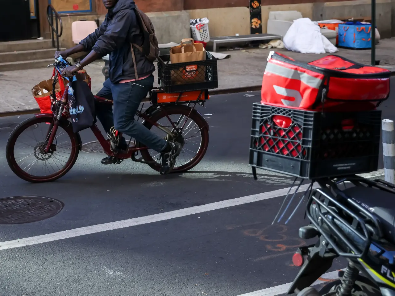 Delivery cyclist with DoorDash bags and crates on a city bike lane