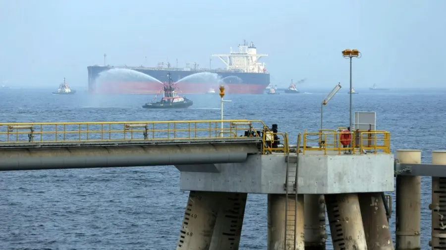 Large oil tanker at sea with tugboats spraying water beside an offshore oil terminal pier.