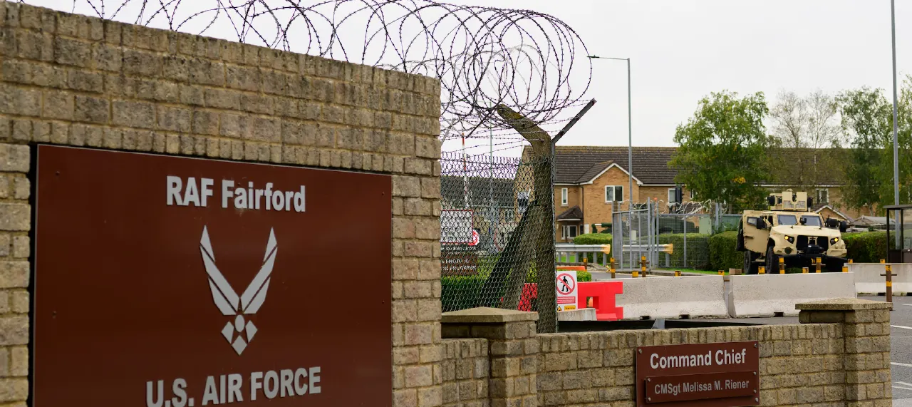 Entrance sign of RAF Fairford, U.S. Air Force base, behind razor wire and a military vehicle.
