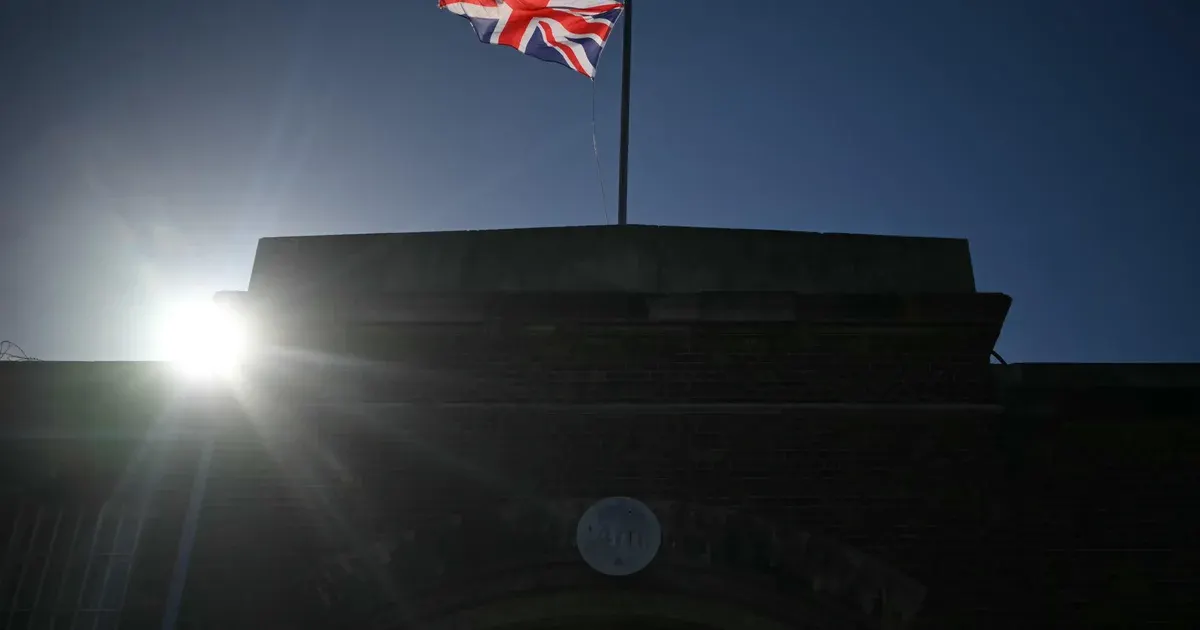 Silhouetted brick building under sun glare with a Union Jack flying from a flagpole.