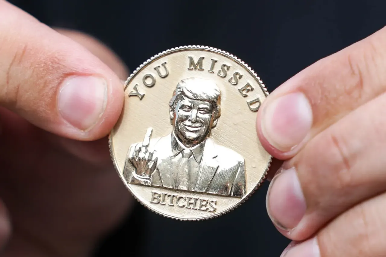 Hands holding a gold coin engraved with a man's bust, middle finger raised, reading YOU MISSED BITCHES