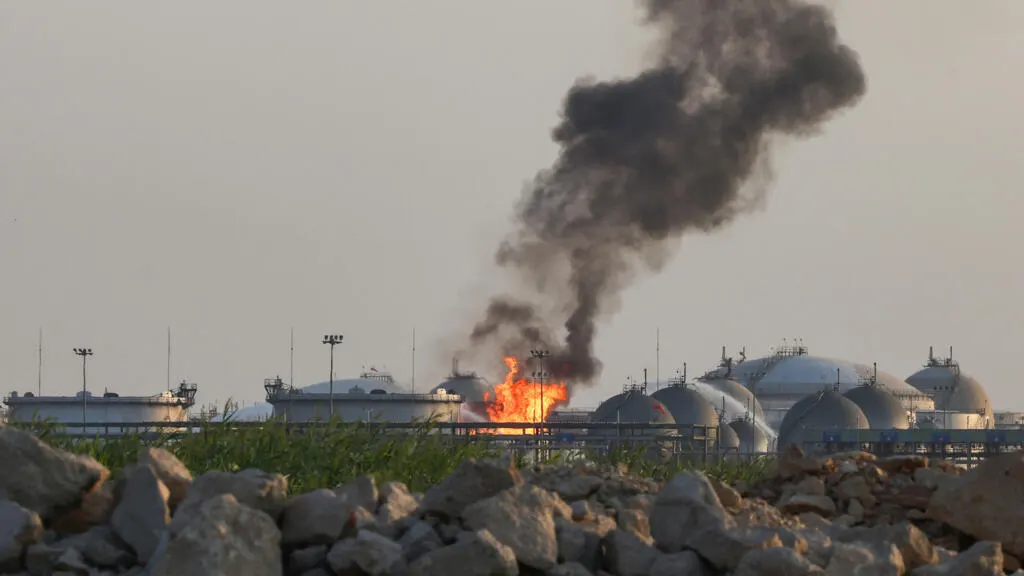 Black smoke and flames rising from white storage tanks at an industrial facility.