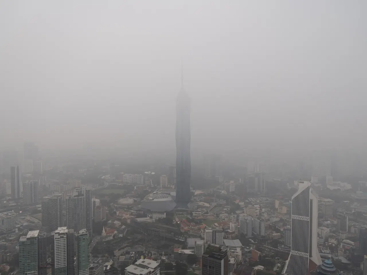 Dense haze shrouds a city skyline with a tall tower in the centre.