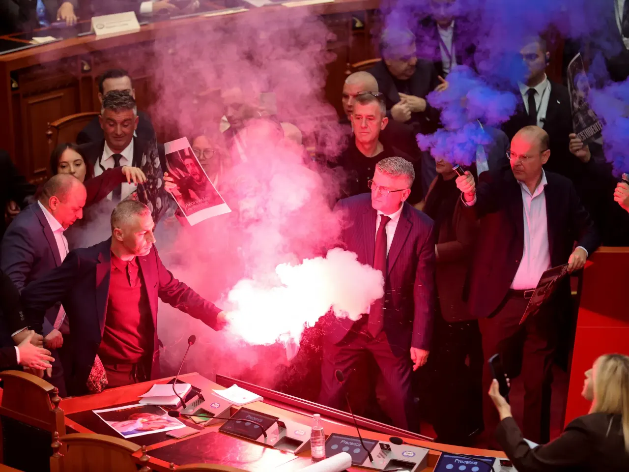 Lawmakers in a parliament chamber, one holding a lit red flare emitting smoke among crowded officials.