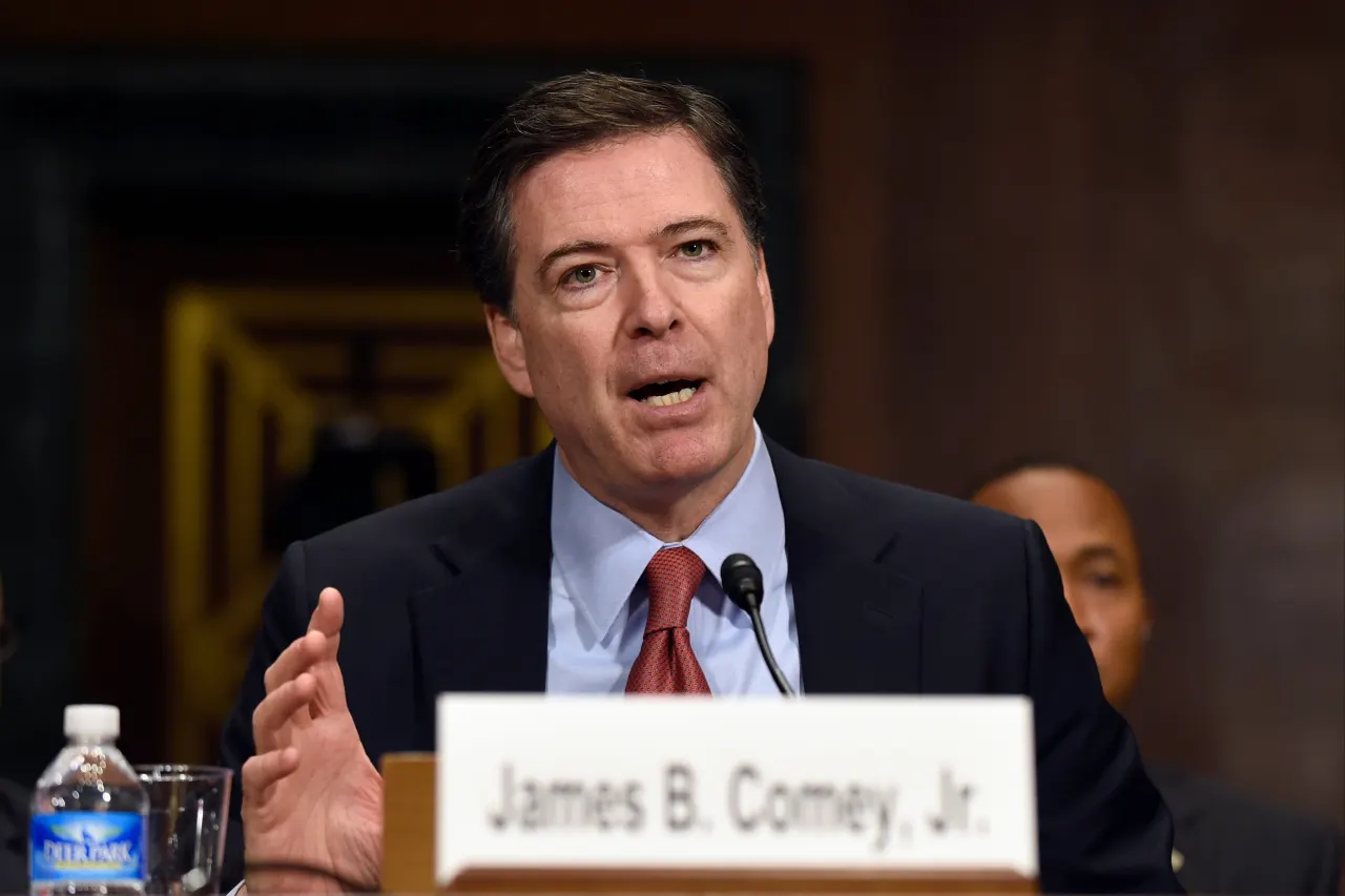 Man in dark suit and red tie speaking at hearing, nameplate reading James B. Comey, Jr.