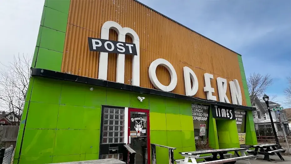 Exterior of a green-and-orange Post Modern restaurant building with outdoor picnic tables and street lamp.