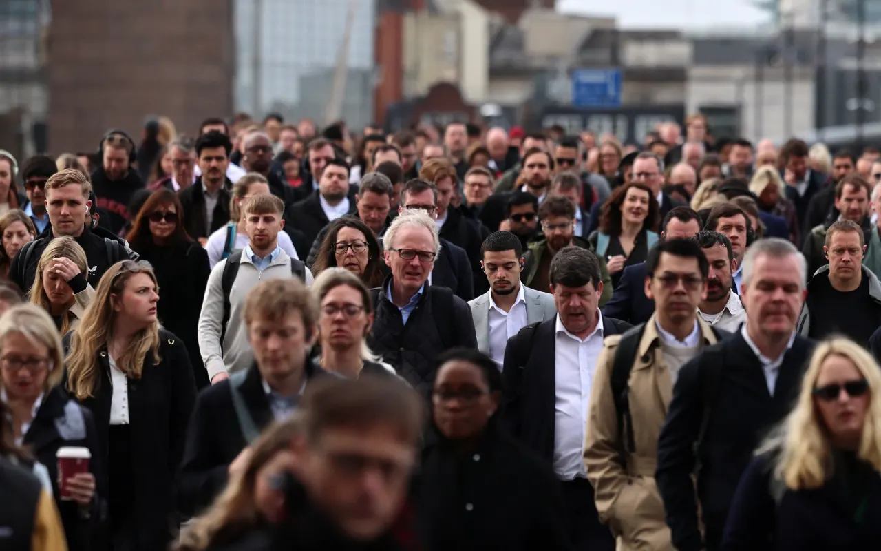 Large crowd of commuters in business attire walking across a city bridge.