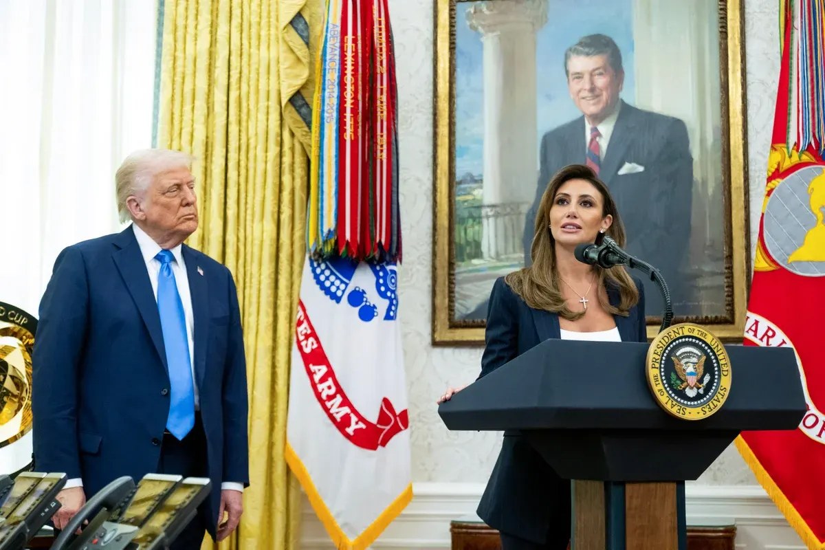 Woman speaks at podium with presidential seal beside a man in formal office setting