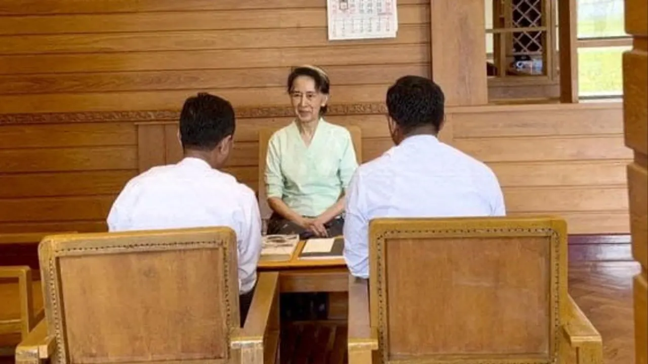 A woman in a pale green blouse sits at a wooden table facing two men with their backs turned.