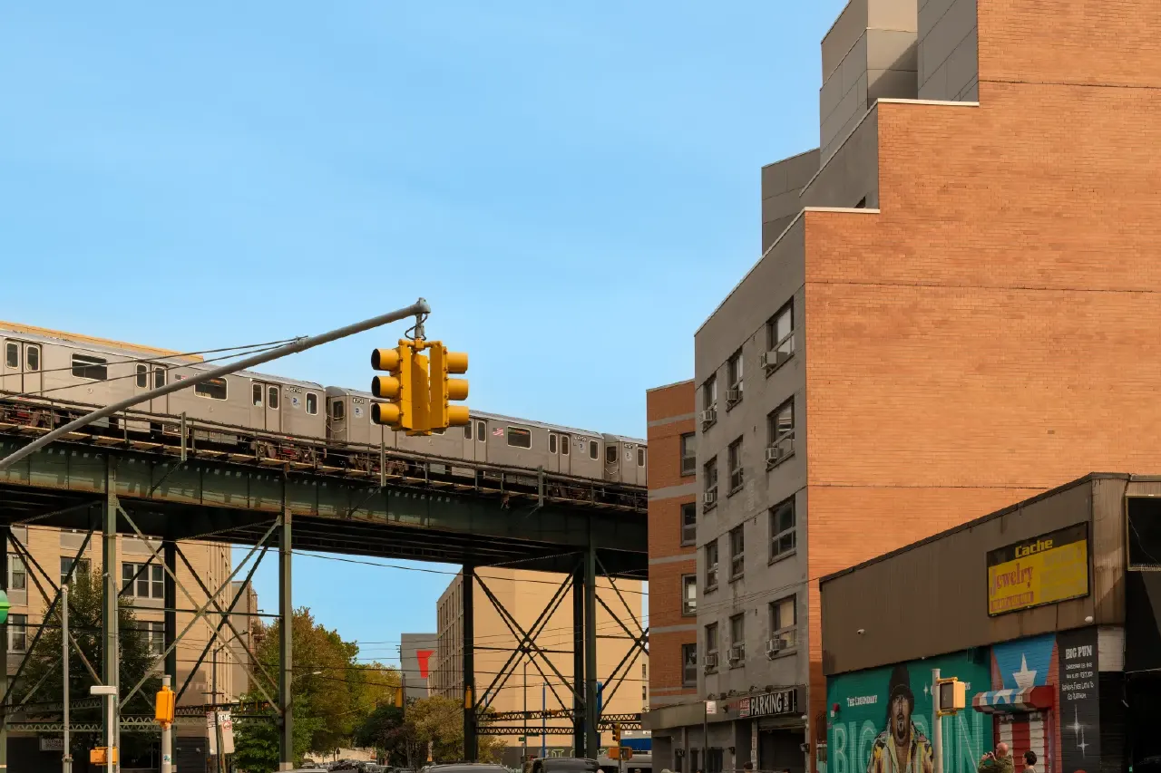 Elevated subway train on a steel trestle above a city street with brick buildings.