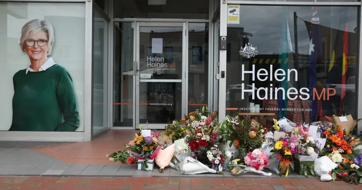 Floral tributes outside Helen Haines MP office storefront, with campaign poster and Australian flag.