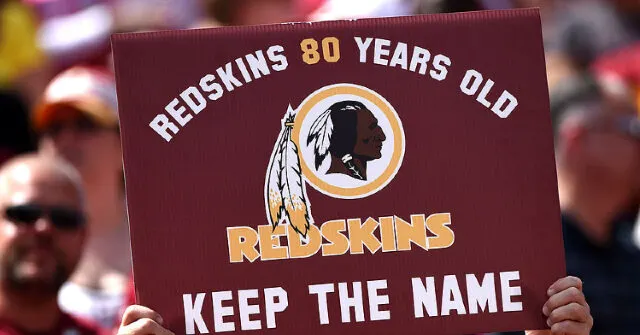 Fan holds maroon sign reading Redskins 80 Years Old, Keep the Name, with team logo, at stadium.