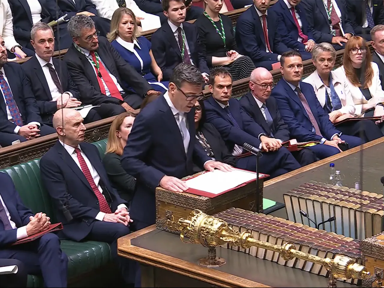 A man in a dark suit speaks at a despatch box in the House of Commons chamber.