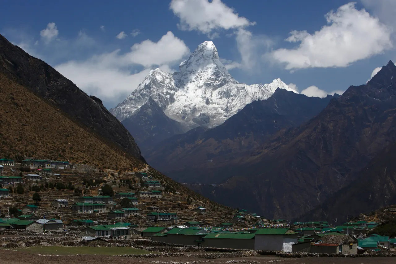 Snow-capped Ama Dablam peak rising above a Himalayan village with green-roofed houses.
