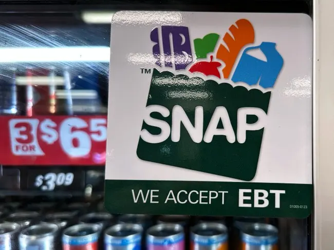 SNAP logo and 'We Accept EBT' sticker on a store window above drinks