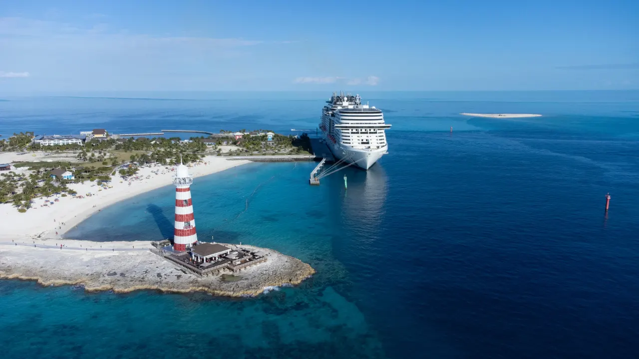 Aerial view of a red-and-white lighthouse, beach and cruise ship in Bahamas waters.