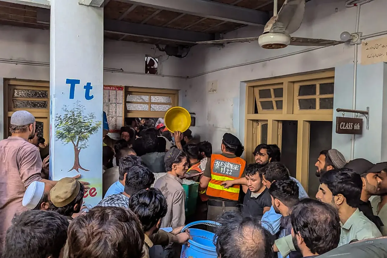 Crowd of men pressing around buckets and a rescue-vested official inside a school corridor.