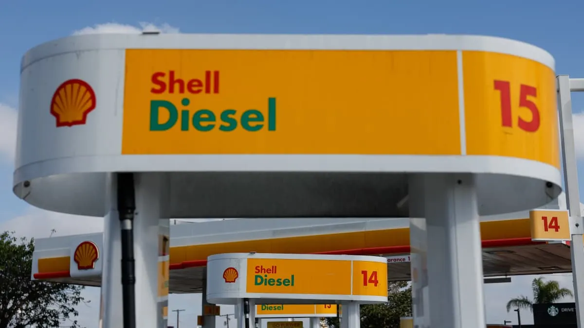 Shell diesel fuel station canopies with pump price signs and yellow-and-red Shell logos under blue sky.