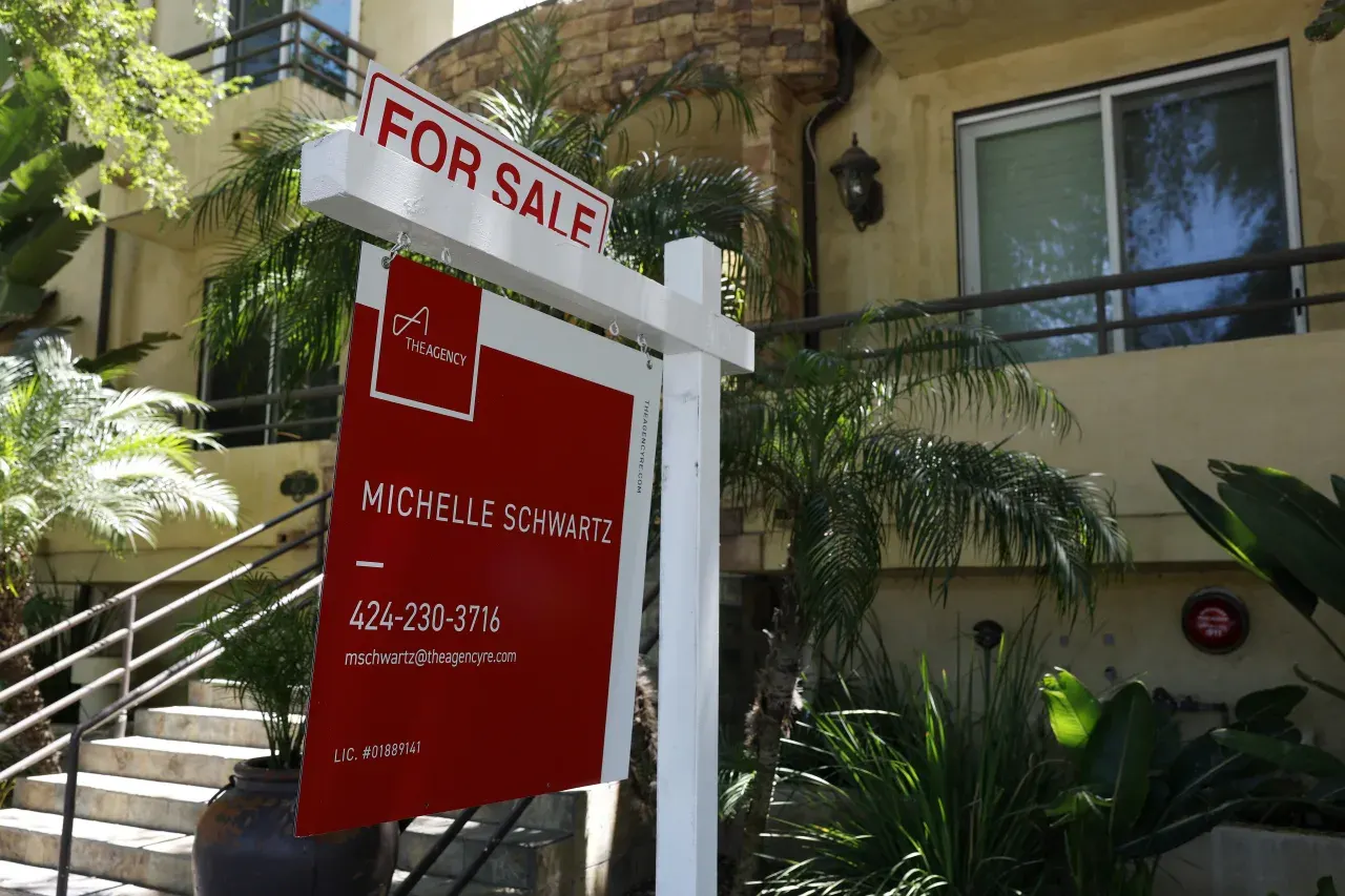 For Sale real estate sign with agent contact details in front of a residential building.