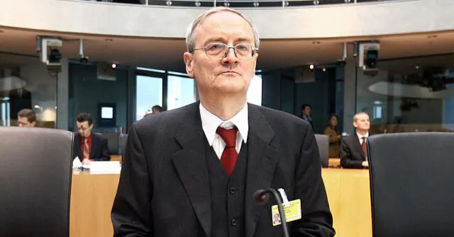 Man in formal business attire seated in an official chamber setting.