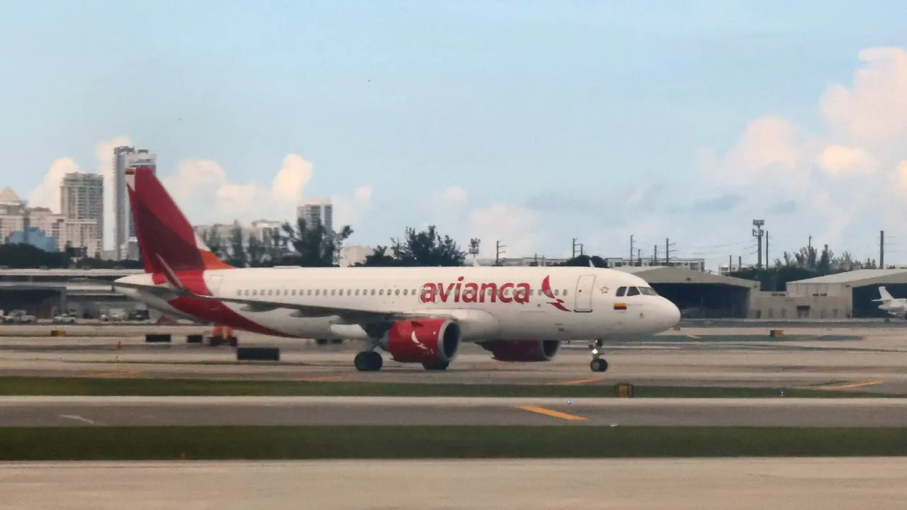 Avianca passenger jet taxiing on airport runway with city skyline behind