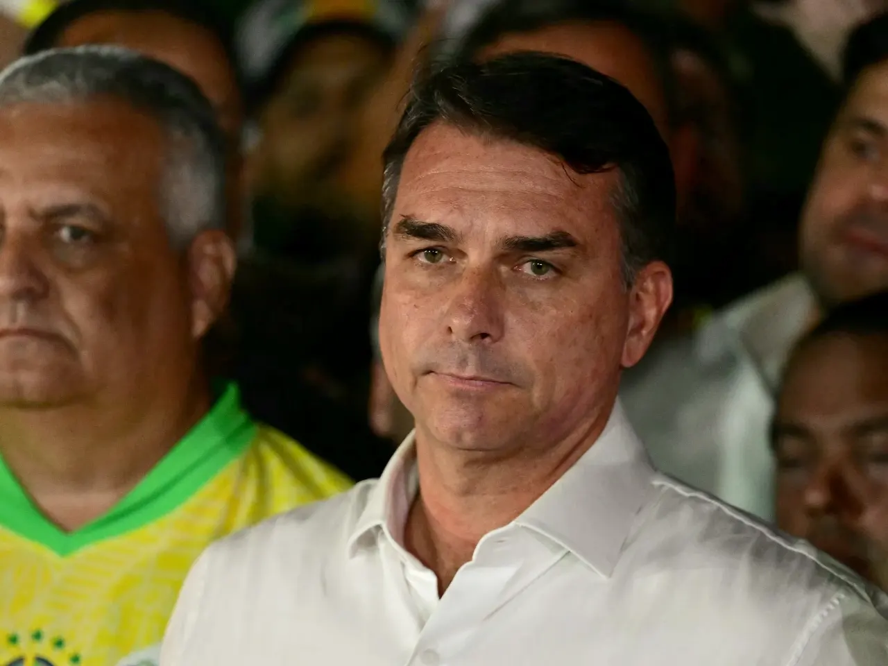 Man in white shirt among crowd, one man in yellow and green jersey beside him