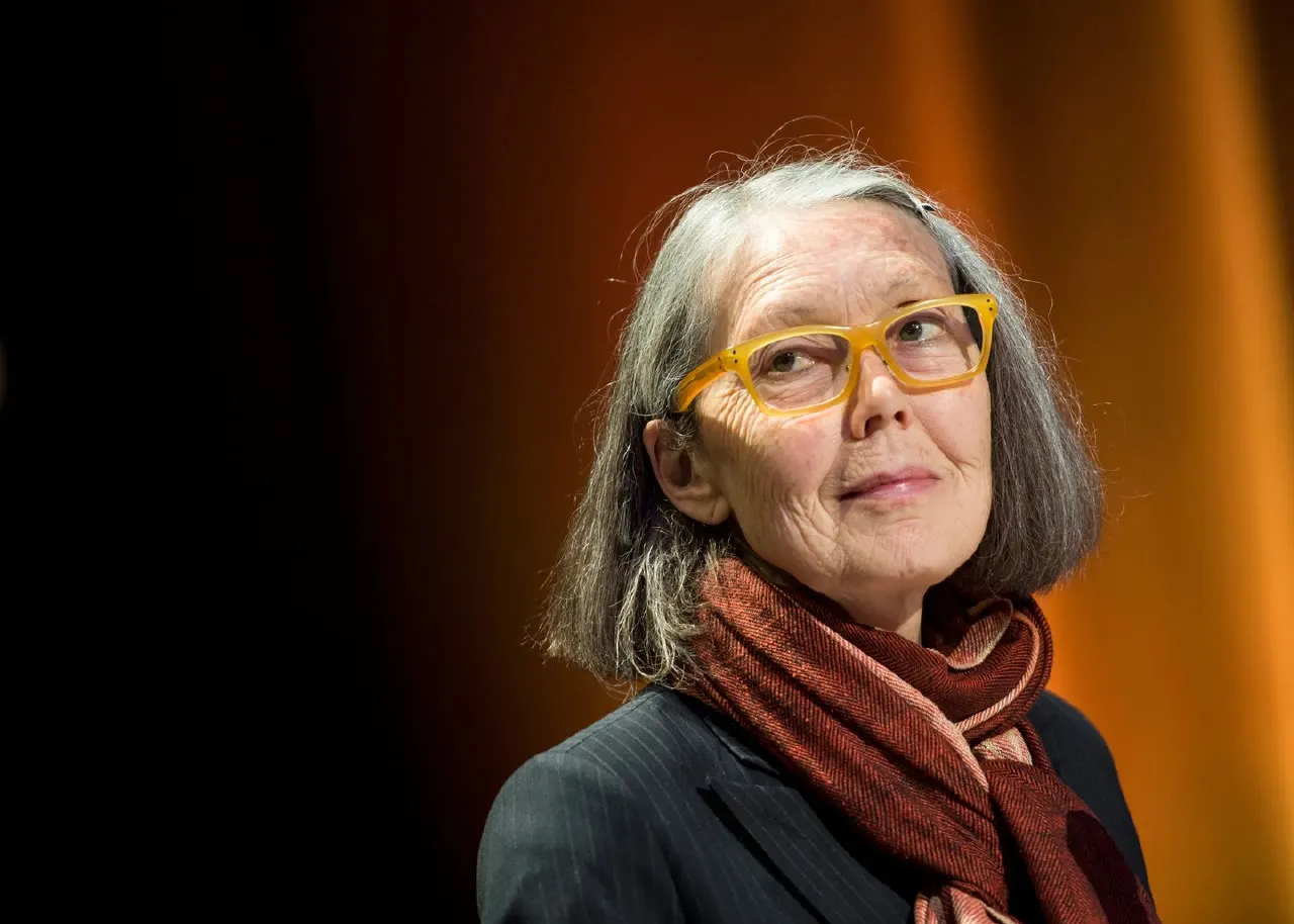 Older woman with grey hair, yellow glasses and red scarf against warm orange backdrop