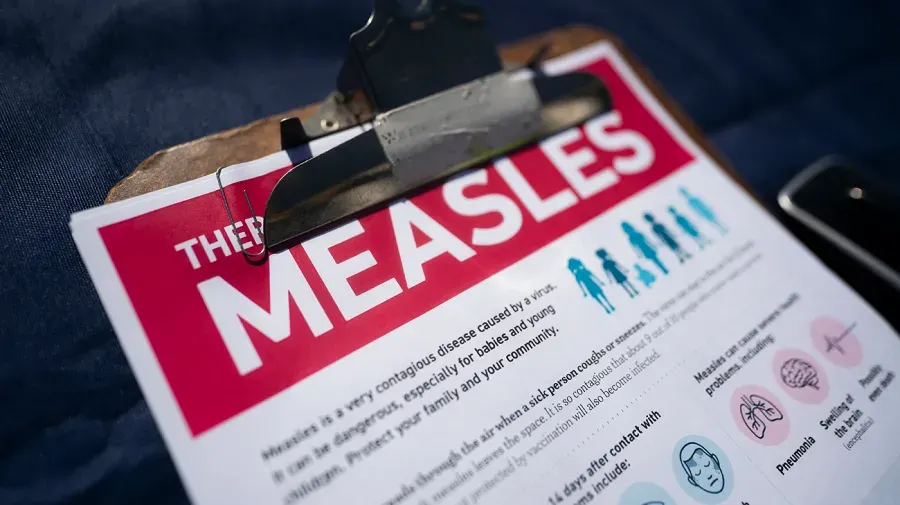 Clipboard with printed measles information sheet showing symptoms and disease facts, shallow focus.