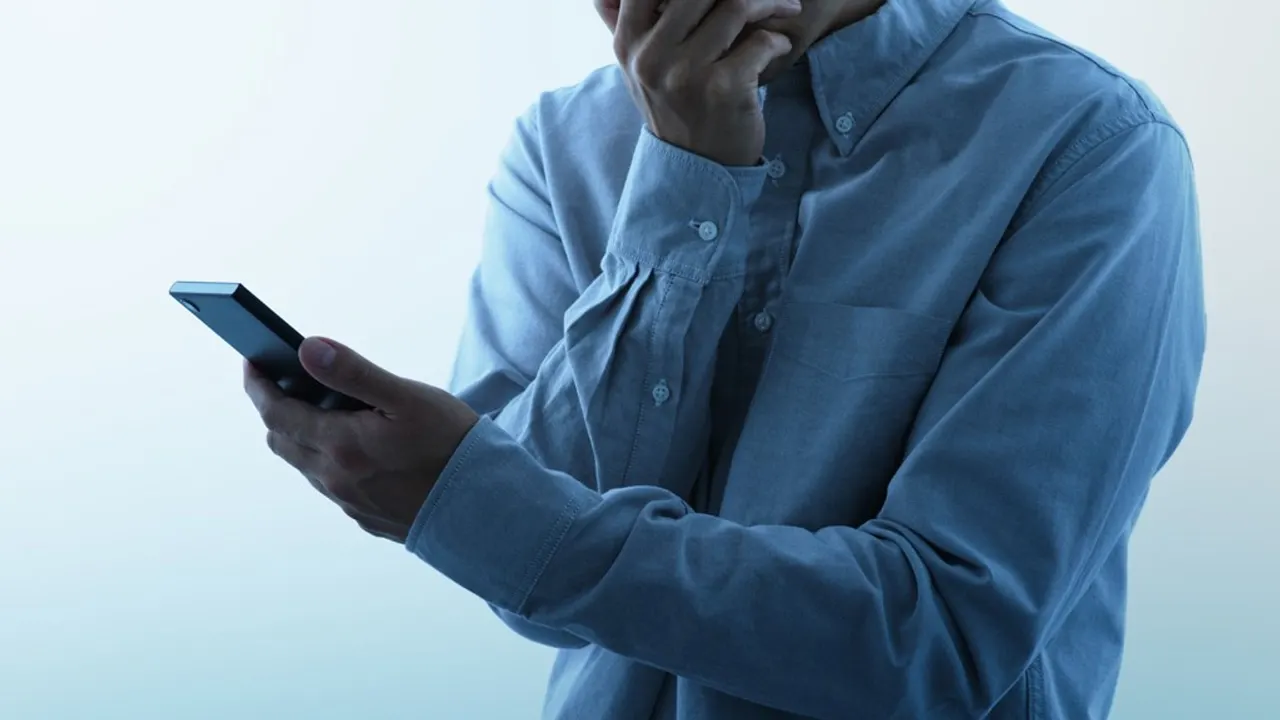 Person in blue shirt looking at smartphone, face cropped out of frame.