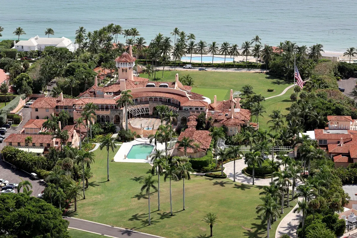 Aerial view of a large Mediterranean-style estate with red roofs, pool and palm trees beside the ocean.