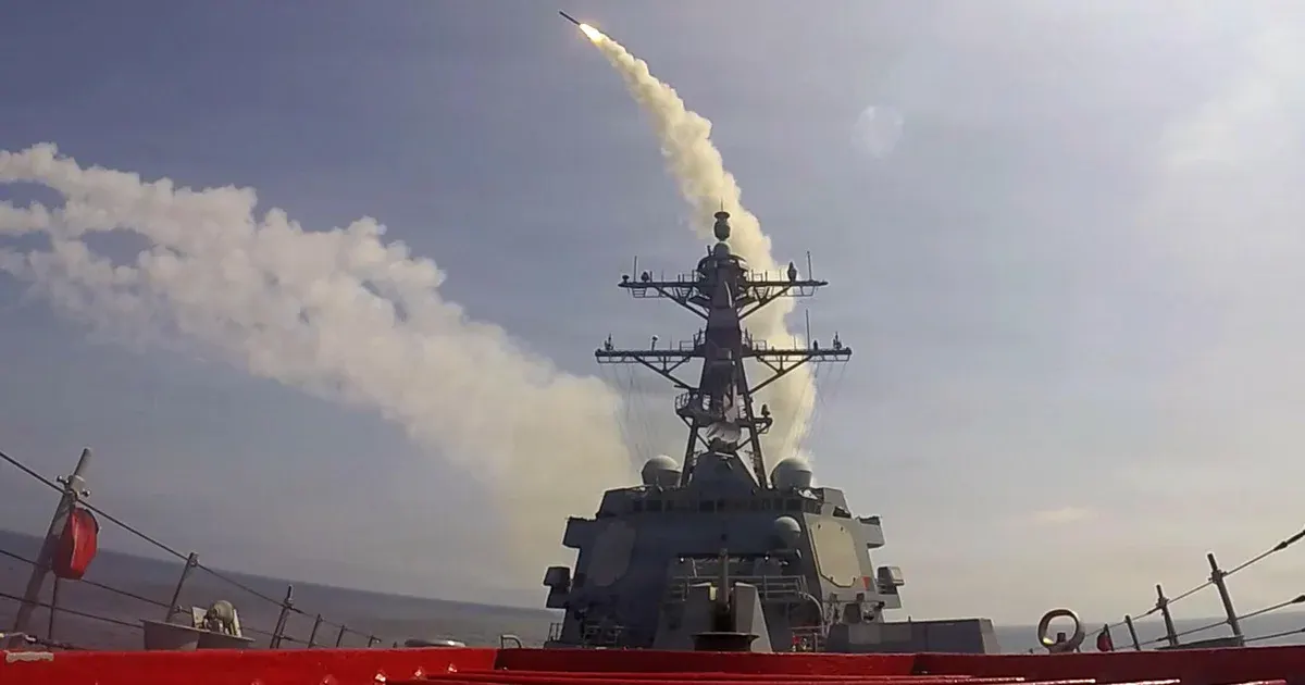 Navy warship on deck firing a missile, smoke trail rising into a hazy sky