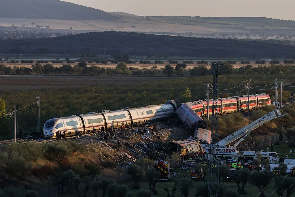 Derailed train cars on embankment with rescue crews and cranes at sunset in rural Spain