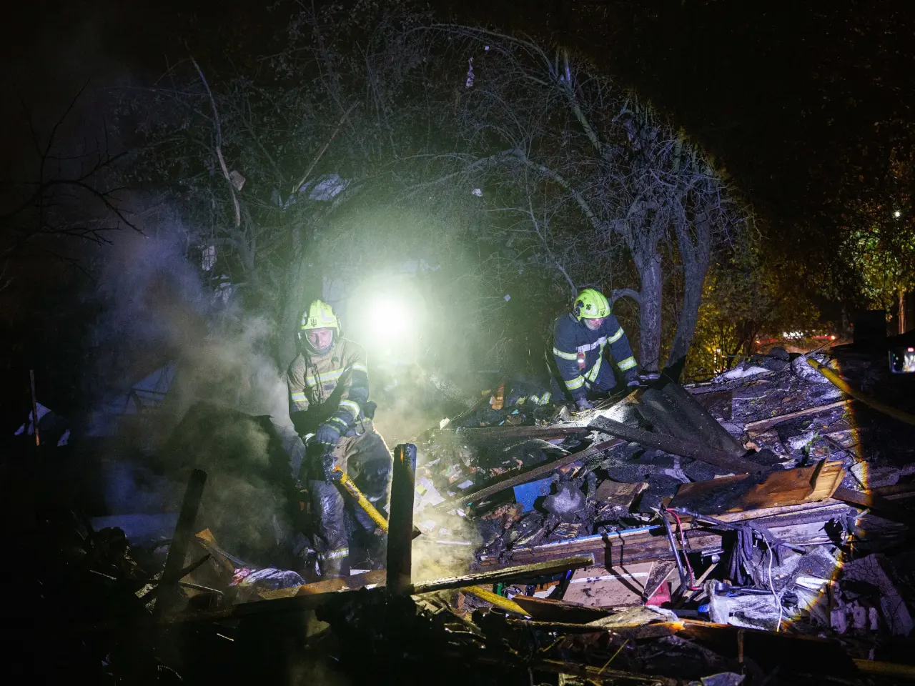Firefighters in helmets search smoldering rubble of a destroyed building at night