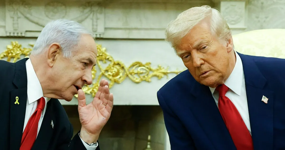 Two men in dark suits and red ties talking indoors before an ornate gold-trimmed fireplace.