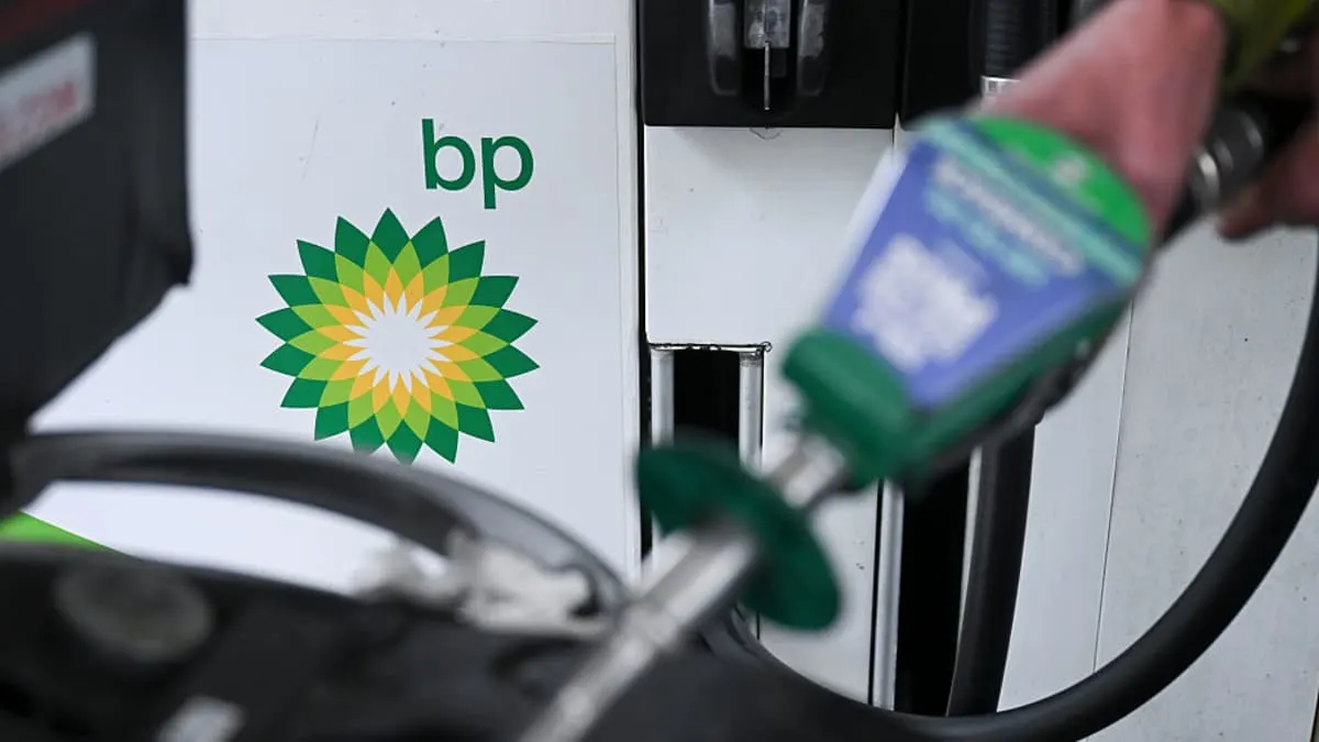 BP logo on a petrol pump as a hand holds a fuel nozzle at a station.