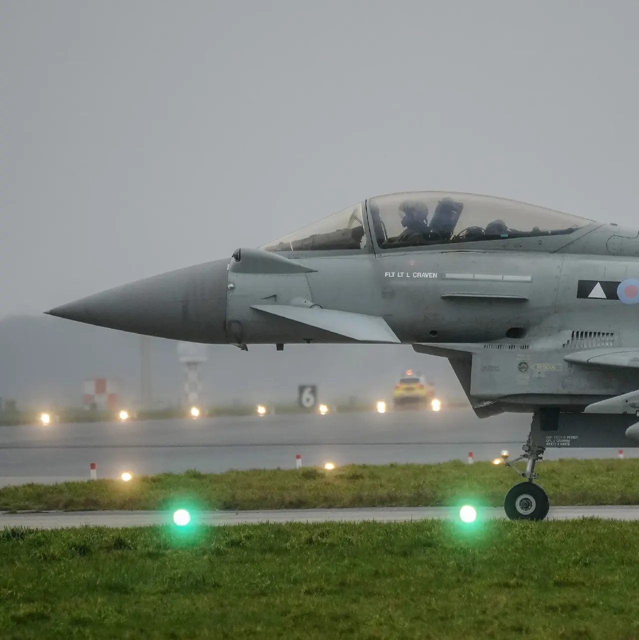 RAF Typhoon fighter jet taxiing on a wet airfield runway at dusk
