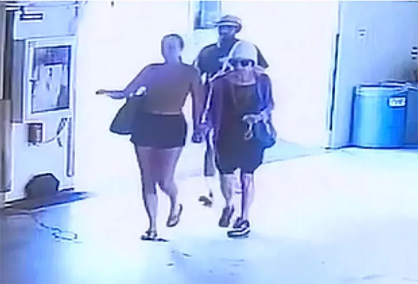 Grainy surveillance footage of two women and a man walking in a garage area.