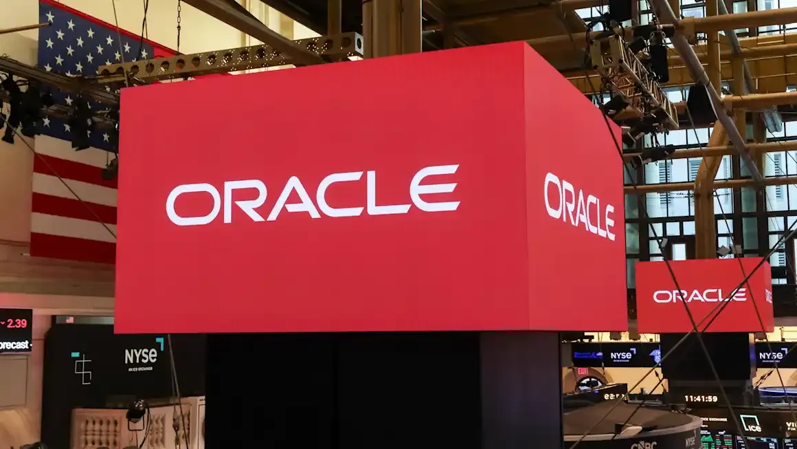 Red Oracle logo signs on a stock exchange trading floor, with NYSE screens and American flag.