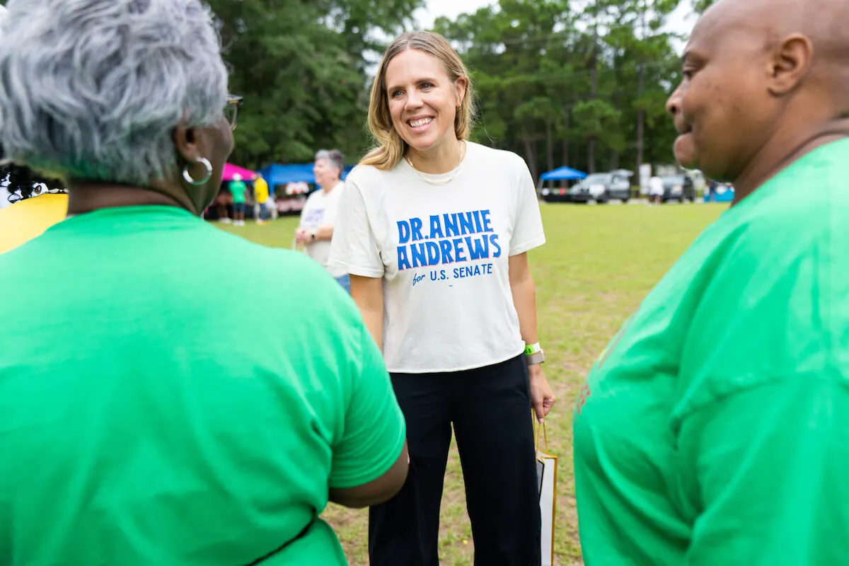 Smiling woman in campaign t-shirt chatting with two people in green outdoors
